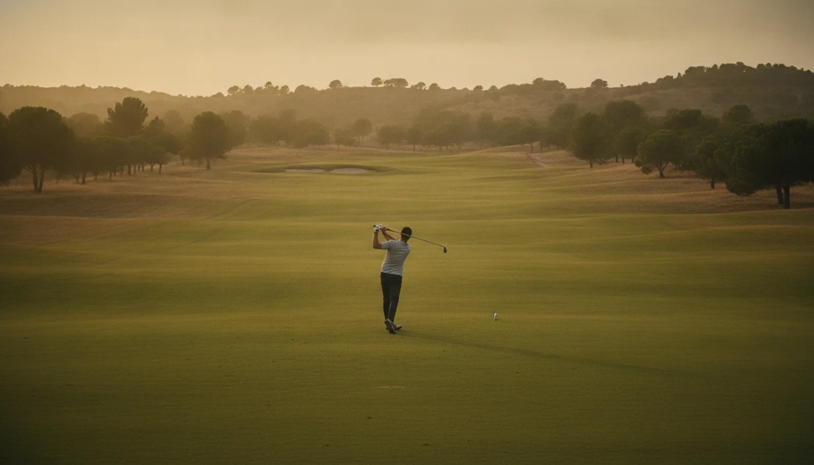 Golfista principiante practicando el swing en una calle amplia a media tarde, visto de lejos
